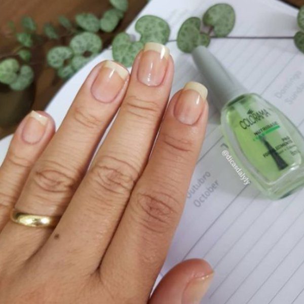 Mão com unhas bem cuidadas sobre agenda, ao lado de esmalte verde claro.