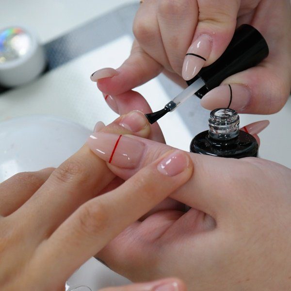Pessoa aplicando esmalte preto em unhas decoradas com linhas coloridas.