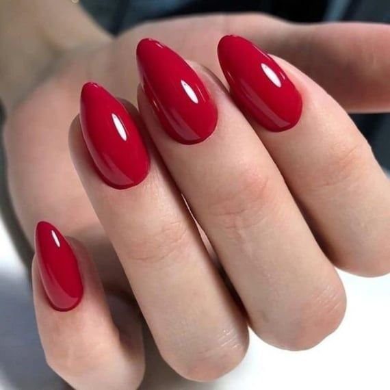 Mão com unhas longas pintadas de vermelho brilhante, destacando-se sobre um fundo neutro.