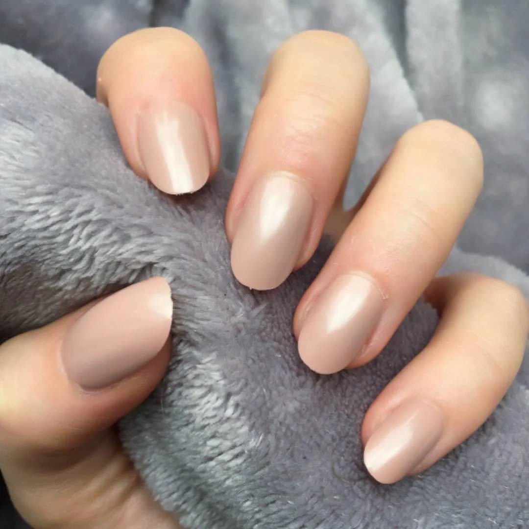 Mão segurando um tecido cinza, com unhas pintadas em tom nude.