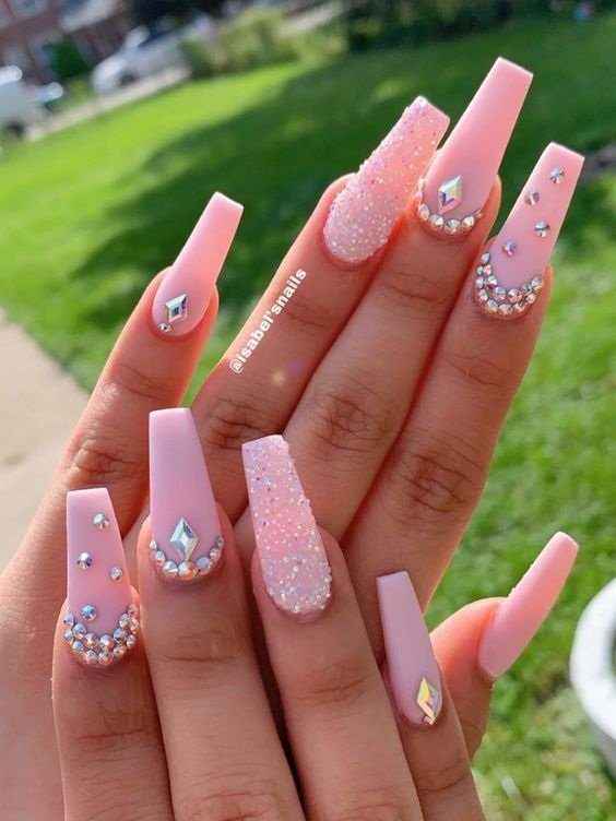 Unhas longas e decoradas com esmalte rosa claro e detalhes em pedrarias brilhantes.