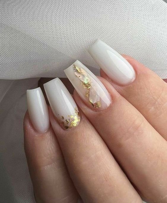 Unhas com esmalte branco e detalhes dourados, mostrando um design elegante e moderno.