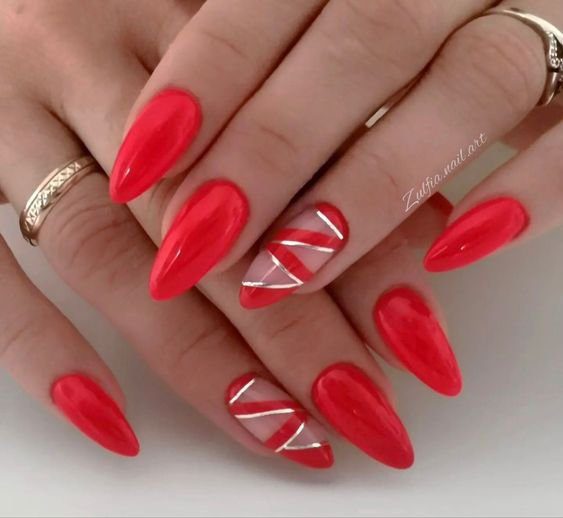 a01730fc4b6c45ae19349d7ce682281e Unhas vermelhas com design geométrico prateado em um dedo, anéis nas mãos.