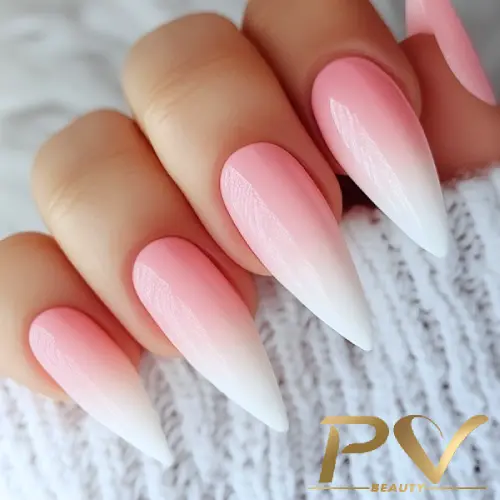 Unhas longas em formato amendoado com esmalte degradê rosa e branco, segurando malha clara.
