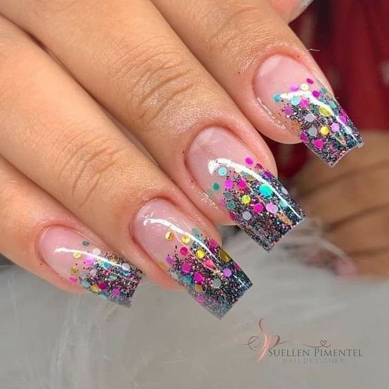 brilho-encapsulado-nas-pontas-e-um-classico-entre-as-inspiracoes-de-unhas-de-carnaval Unhas decoradas com glitter e pequenos pontos coloridos em um estilo moderno e vibrante.