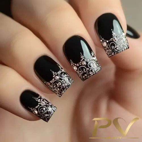Unhas decoradas com esmalte preto e desenhos prateados detalhados nas pontas.