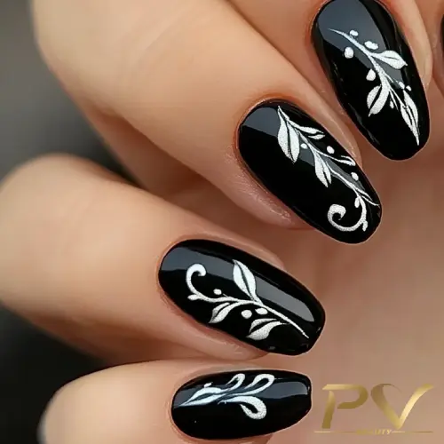 Unhas decoradas com esmalte preto e desenhos prateados de folhas e arabescos.