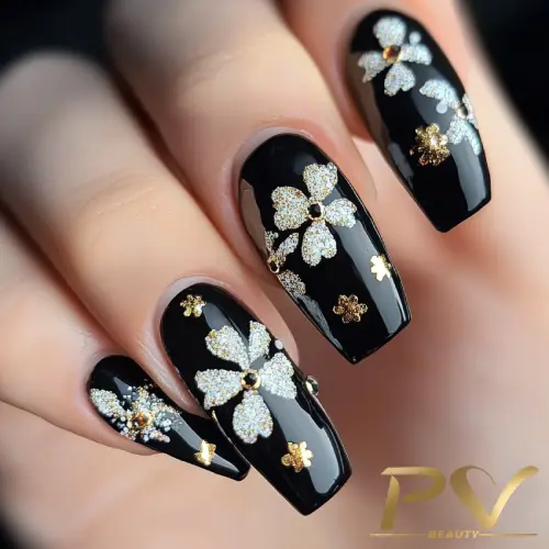 Unhas com esmalte preto e decoração de flores douradas e prateadas.