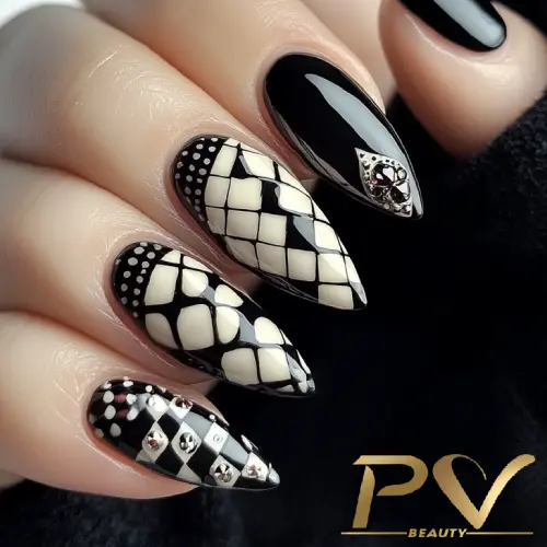 Unhas decoradas em preto e branco com padrões geométricos e detalhes metálicos.