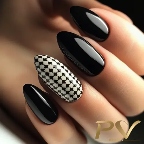 Unhas longas e pontudas com esmalte preto brilhante e uma unha decorada com padrão geométrico preto e branco.
