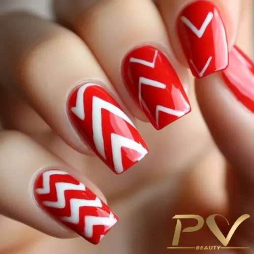 Unhas vermelhas com desenhos geométricos brancos em ziguezague e chevron, exibindo um design moderno e elegante.