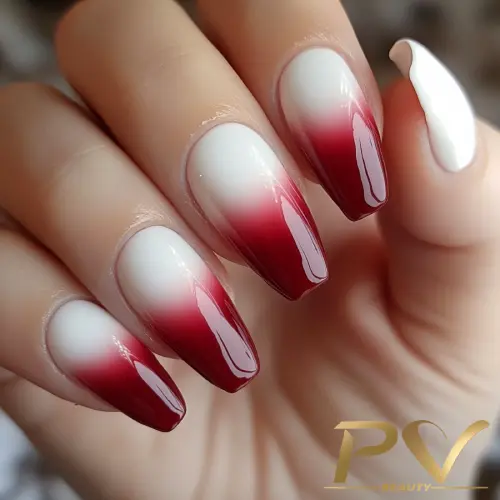 Unhas decoradas com esmalte degradê em tons de branco e vermelho, em uma mão segurando o polegar oposto.