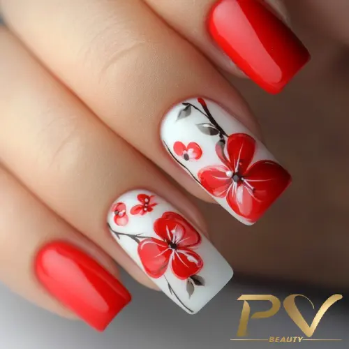 Unhas decoradas com esmalte vermelho e desenhos florais em fundo branco.