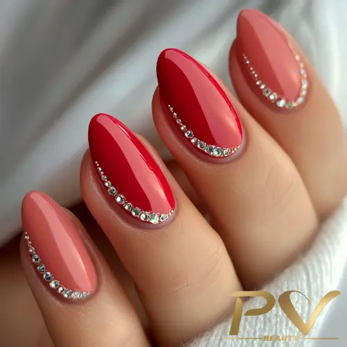 Unhas decoradas em tons de vermelho e rosa com aplicação de pedrarias prateadas na base.
