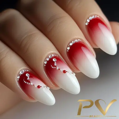Unhas com esmalte gradiente vermelho e branco, decoradas com pequenas pedras brilhantes.