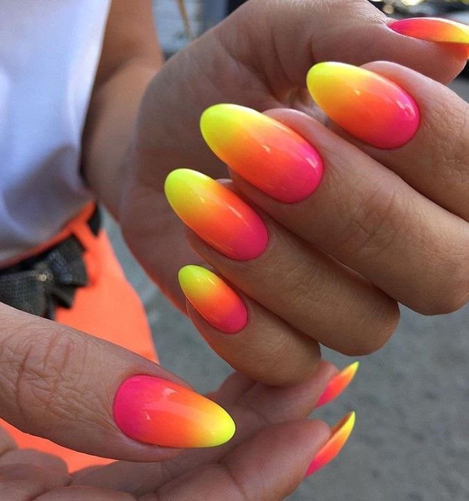 degrade-colorido-foto-pinterest Mãos com unhas decoradas em efeito degradê de cores neon, variando entre amarelo, laranja e rosa.