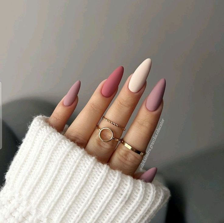 Unhas longas e pontudas com esmalte fosco em tons de rosa e nude, acompanhadas por anéis delicados.