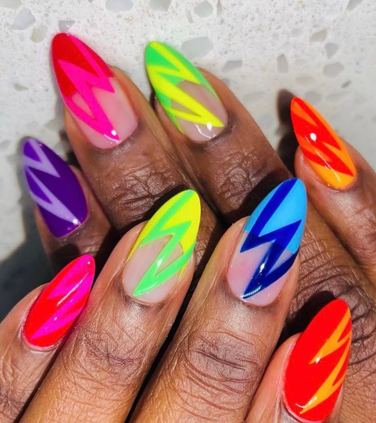 Unhas com esmalte colorido em design geométrico, com cores vibrantes como vermelho, azul, verde e laranja.