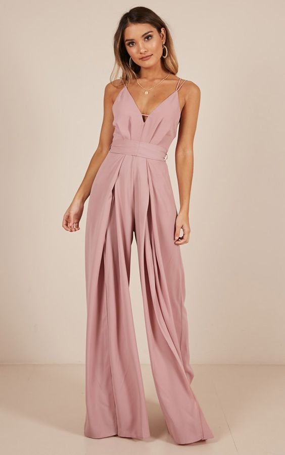 Pessoa usando um macac&atilde;o rosa de al&ccedil;as finas, posando em fundo neutro.