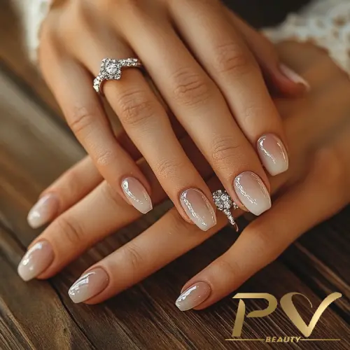 Mãos cruzadas com unhas decoradas e dois anéis de diamante sobre uma superfície de madeira.