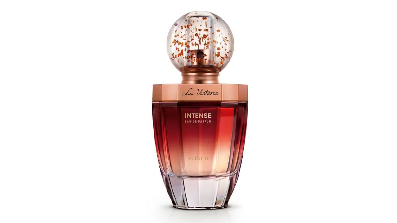 Frasco de perfume com design elegante, tampa redonda transparente e líquido em tons de vermelho e dourado.