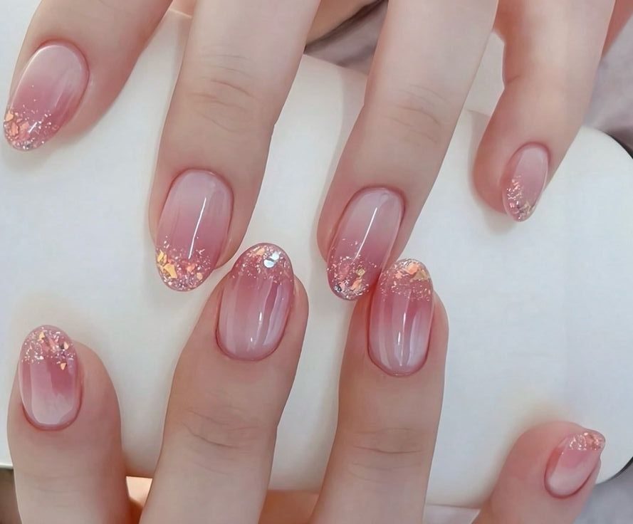 Unhas com esmalte rosa claro e glitter prateado nas pontas, em um fundo branco.