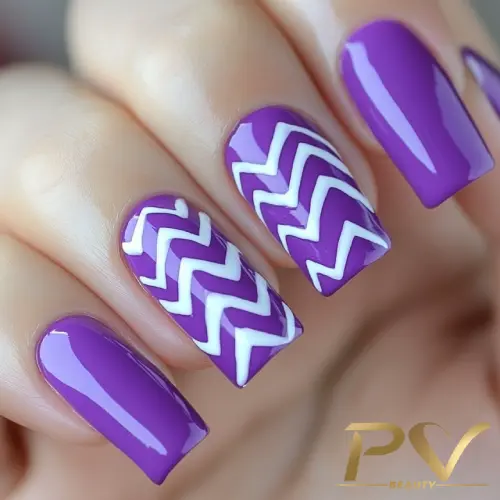 roxo-unhas-chevron-decoradas-pv-beauty-06 Unhas com esmalte roxo e padrão de zigue-zague branco em duas delas, mostrando um design de nail art moderno.