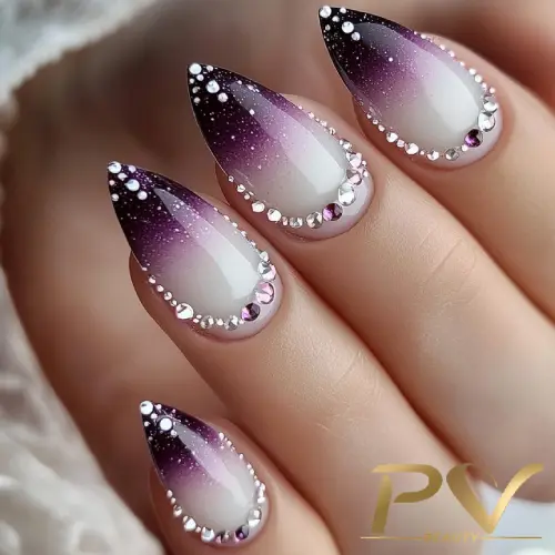 roxo-unhas-decoradas-strass-lindas-pv-beauty-32 Unhas em formato pontiagudo com esmalte degradê roxo e pedras decorativas prateadas ao redor.