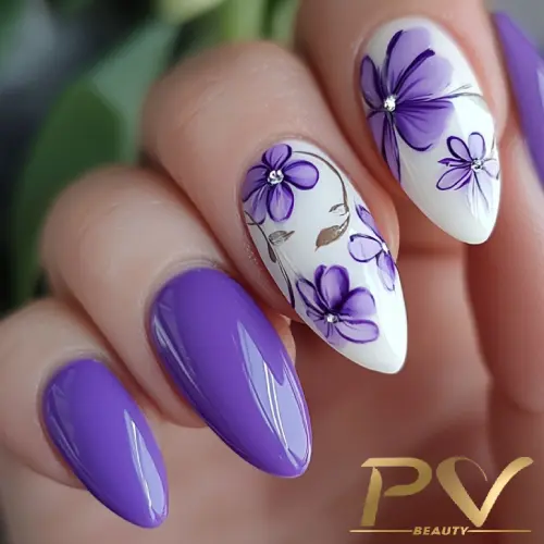 roxo-unhas-floral-decoradas-pv-beauty-10 Unhas decoradas com esmalte roxo e flores desenhadas em branco e roxo, com pequenos detalhes prateados.