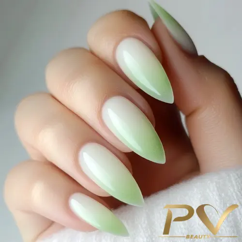 Unhas em formato amendoado com esmalte em degradê verde claro, segurando um tecido branco.