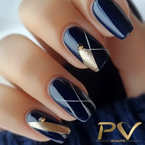 Unhas pintadas de azul escuro com detalhes geométricos em dourado e branco.