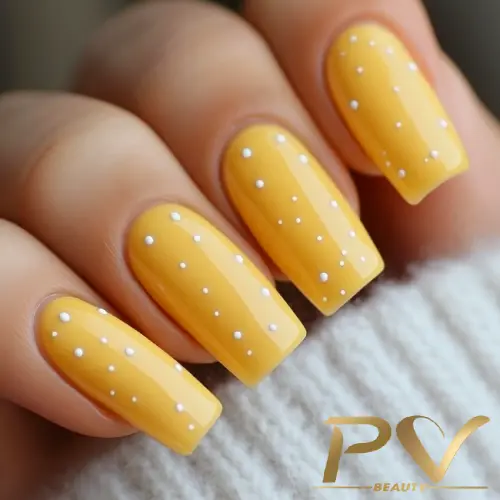 unha-de-gel-perto-de-mim-decorada-amarela-poa-pv-beauty-07 Unhas amarelas compridas com pequenos pontos brancos, segurando um tecido claro.