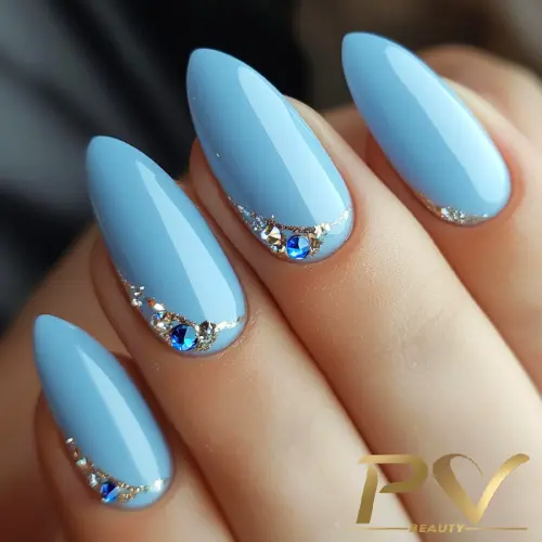 unha-de-gel-perto-de-mim-decorada-azul-strass-pv-beauty-05 Unhas azuis com pedras azuis e detalhes prateados brilhantes, em formato amendoado.