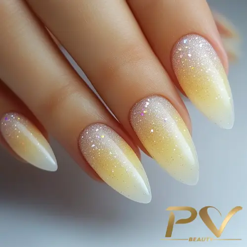 Unhas em formato stiletto com esmalte em degradê amarelo e glitter brilhante.