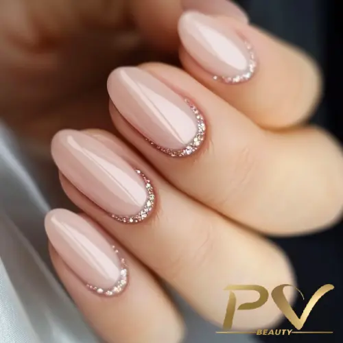 Unhas com esmalte nude e bordas decoradas com glitter dourado.