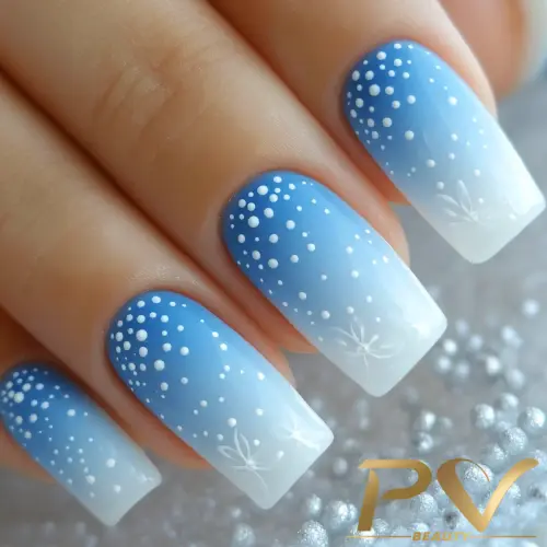 Unhas com esmalte azul e branco em degradê, decoradas com pequenos pontos brancos e desenhos delicados.