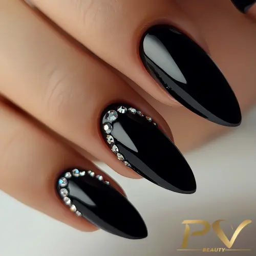 Unhas compridas com esmalte preto brilhante e detalhes em pedras brilhantes.