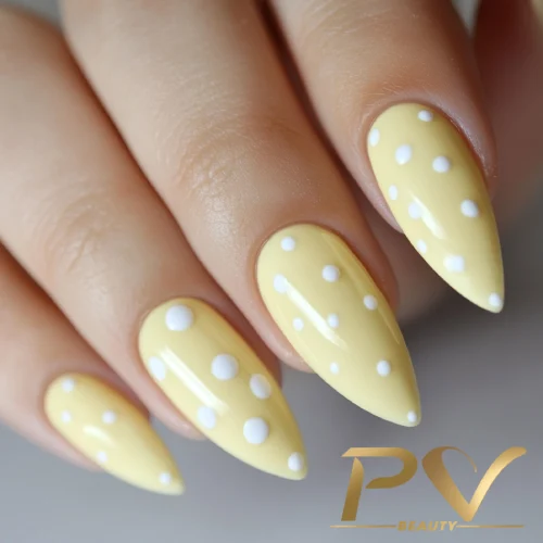 unhas-amarelas-bolinhas-brancas-decoradas-pv-beauty-25 Unhas decoradas com esmalte amarelo e bolinhas brancas sobre fundo neutro.