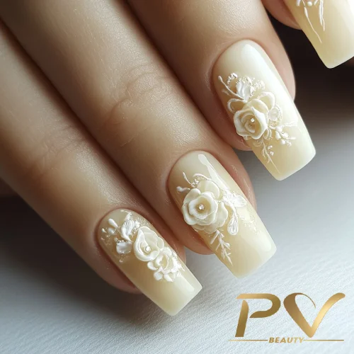 unhas-amarelas-floral-decoradas-pv-beauty-22 Unhas em tom nude com decoração floral em relevo branco, exibindo detalhes delicados e elegantes.