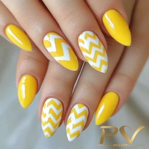 unhas-amarelas-zig-zag-decoradas-pv-beauty-30 Unhas com esmalte amarelo e padrão geométrico branco, estilo zigue-zague.