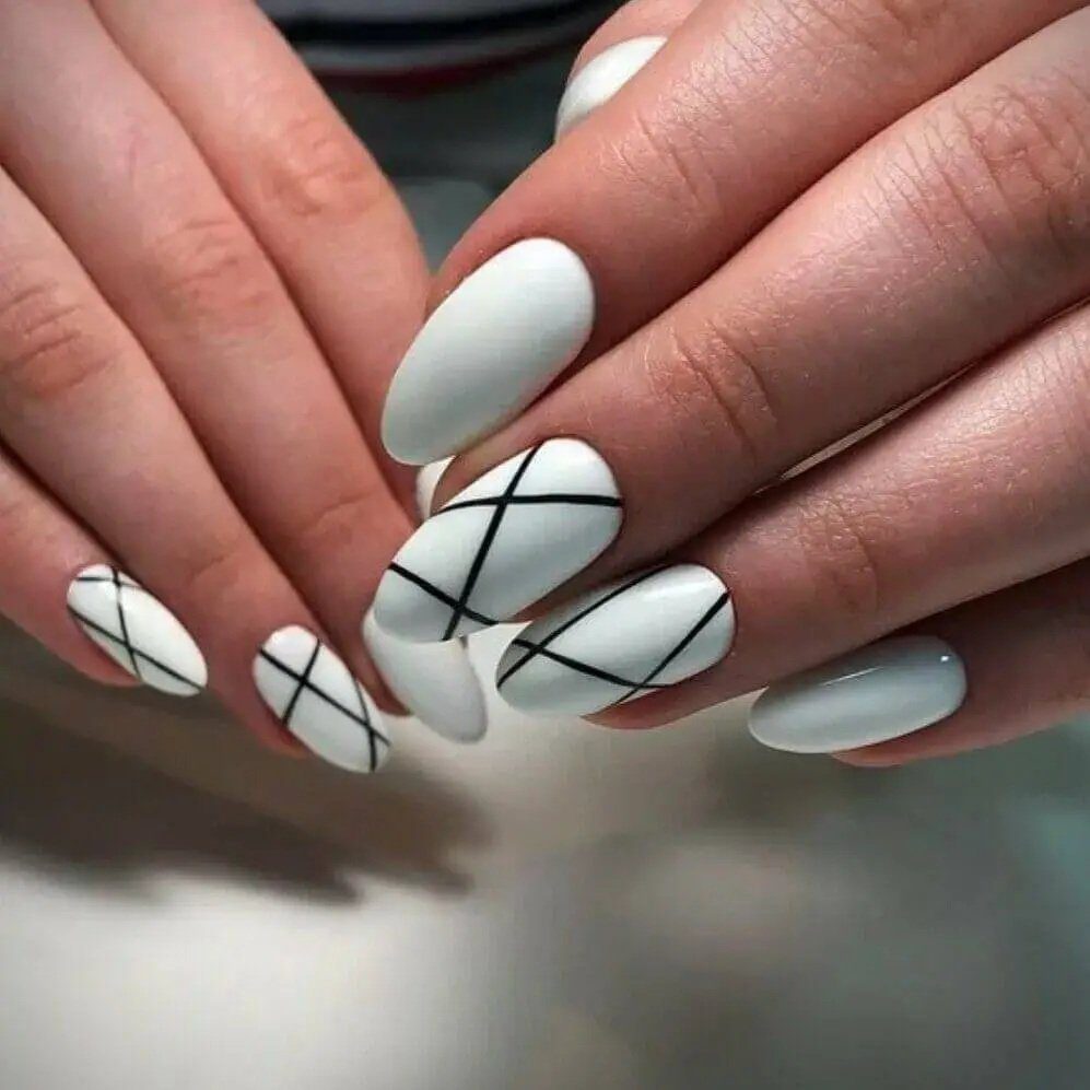 Unhas pintadas de branco com linhas pretas cruzadas, formando um design geométrico elegante.