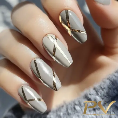 unhas-cinza-decorada-metais-dourados-pv-beauty-16 Unhas decoradas com esmalte cinza e detalhes dourados em linhas diagonais, em uma mão segurando tecido cinza.