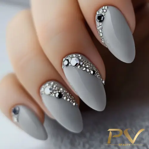 unhas-cinza-decorada-strass-pv-beauty-21 Unhas decoradas em tom cinza com pedras prateadas e pretas, formando um design elegante e sofisticado.