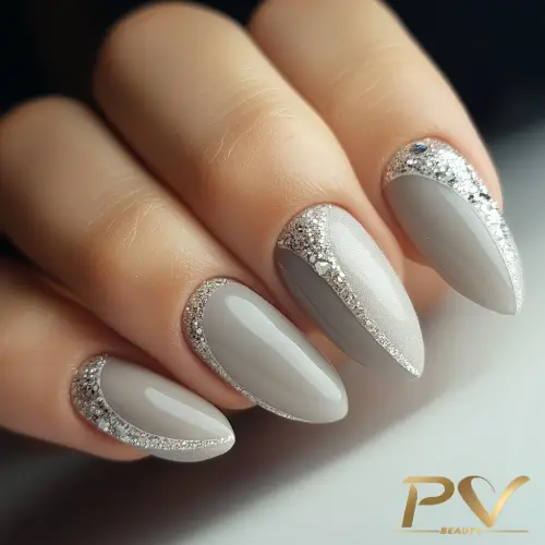 unhas-cinza-glitter-finas-pedrarias-design-lindo-pv-beauty-18 Unhas com esmalte cinza e detalhes em glitter prateado nas bordas, em um fundo neutro.