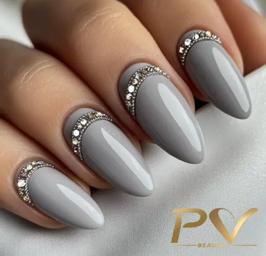 unhas-cinza-pedrarias-brilho-lindo-glamour-pv-beauty-35 Unhas pintadas de cinza claro com decoração de pedrarias prateadas na base, sobre um fundo claro.