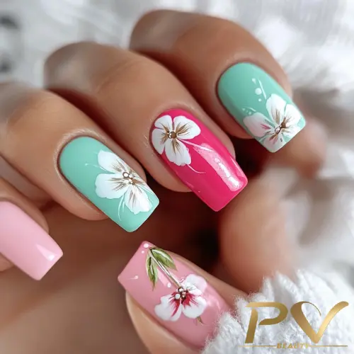 Unhas decoradas com esmalte rosa e verde, adornadas com desenhos de flores brancas e detalhes delicados.