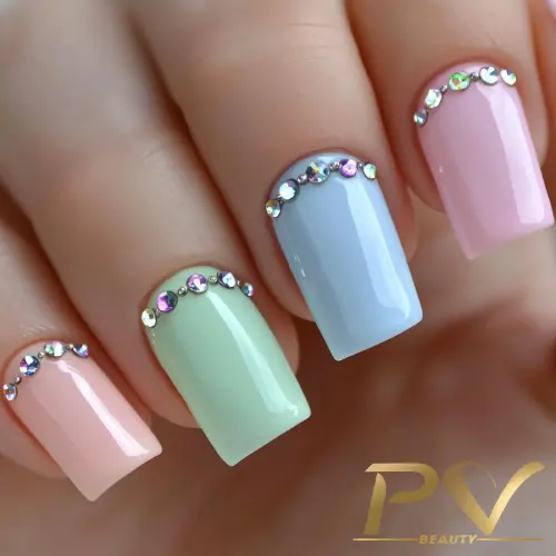 Unhas decoradas com esmalte em tons pastel e pedras brilhantes na base de cada unha.