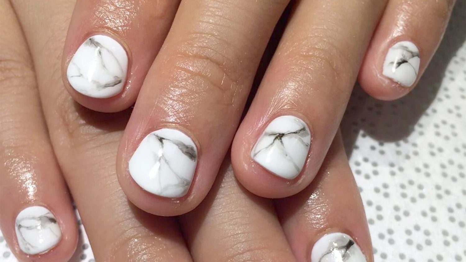 Unhas curtas com esmalte branco em design marmorizado, com detalhes em cinza e preto.