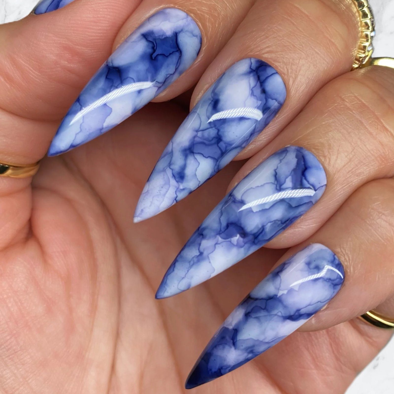 Unhas compridas com design marmorizado em tons de azul e branco, com formato pontiagudo.