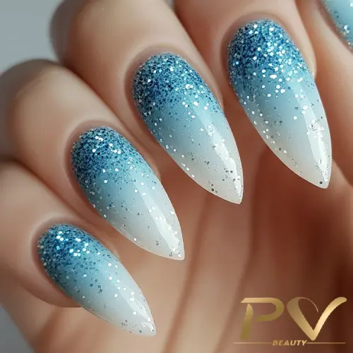 unhas-decorada-azul-glitter-sofisticado-pv-beauty-33 Unhas pontiagudas com esmalte em degradê azul e glitter prateado, destacando um design elegante e brilhante.